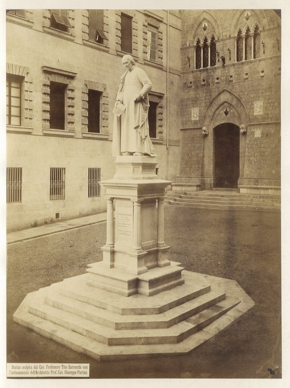 (FOTOGRAFIA: Paolo LOMBARDI - SALLUSTIO BANDINI). Grande fotografia (mm. 345 x 260) in b.n., databile alla fine del sec. XIX: come da legenda in basso a sinistra della foto, raffigura la "statua di Sallustio Bandini scolpita dal Cav. Prof. Tito Sarrocchi con l'imbasamento dell'Arch. Prof. Cav. Giuseppe Partini". Presa di 3/4, all'angolo fra il gotico Palazzo Salimbeni, di cui si vede il portale e 2 trifore sotto gli archi a sesto acuto e Palazzo Tantucci del Riccio (sec. XVI).
