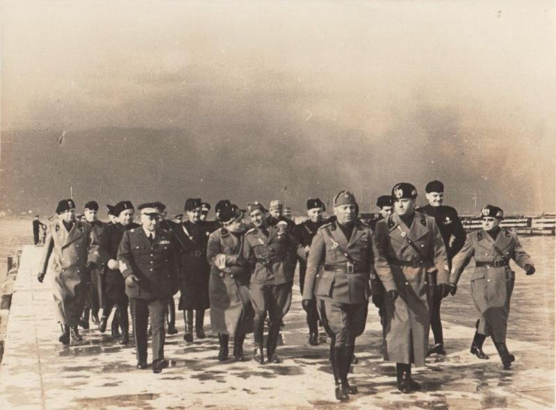 Il Duce con altri gerarchi in cammino lungo un molo. | Immagine principale